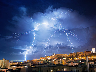 Ein Blitzschauer über einer Stadt bei Nacht, mit dramatischem Himmel.